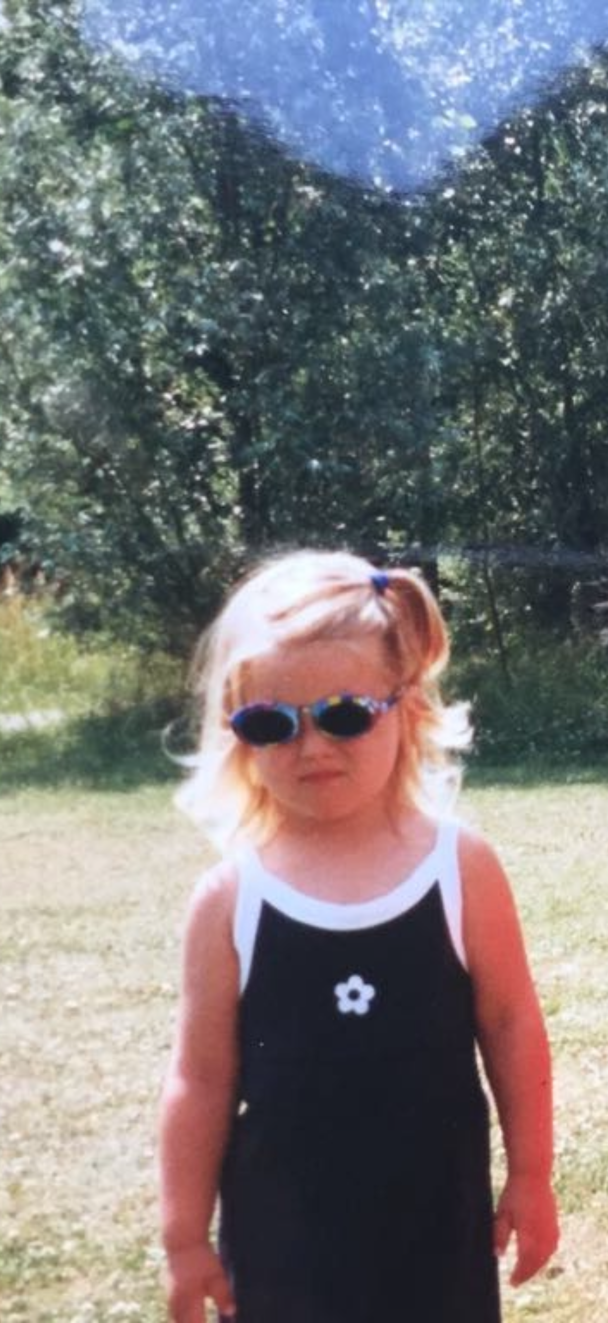 A little girl in sunglasses standing outside with a very serious expression