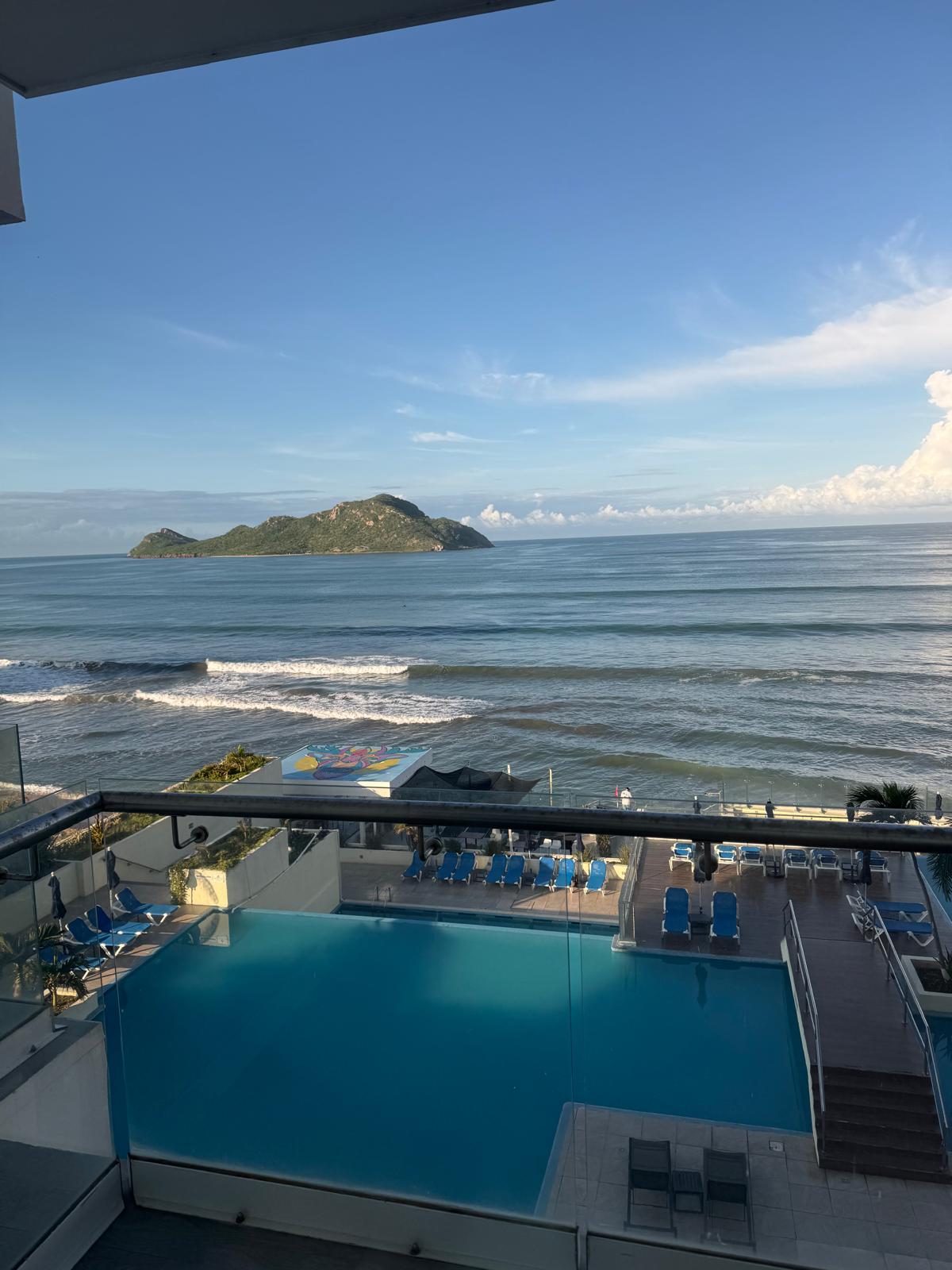 Ocean view from a hotel balcony with a pool and a small island offshore